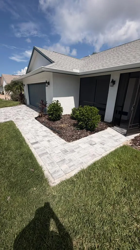 Freshly painted white stucco home with dark trim beside a new paver walkway