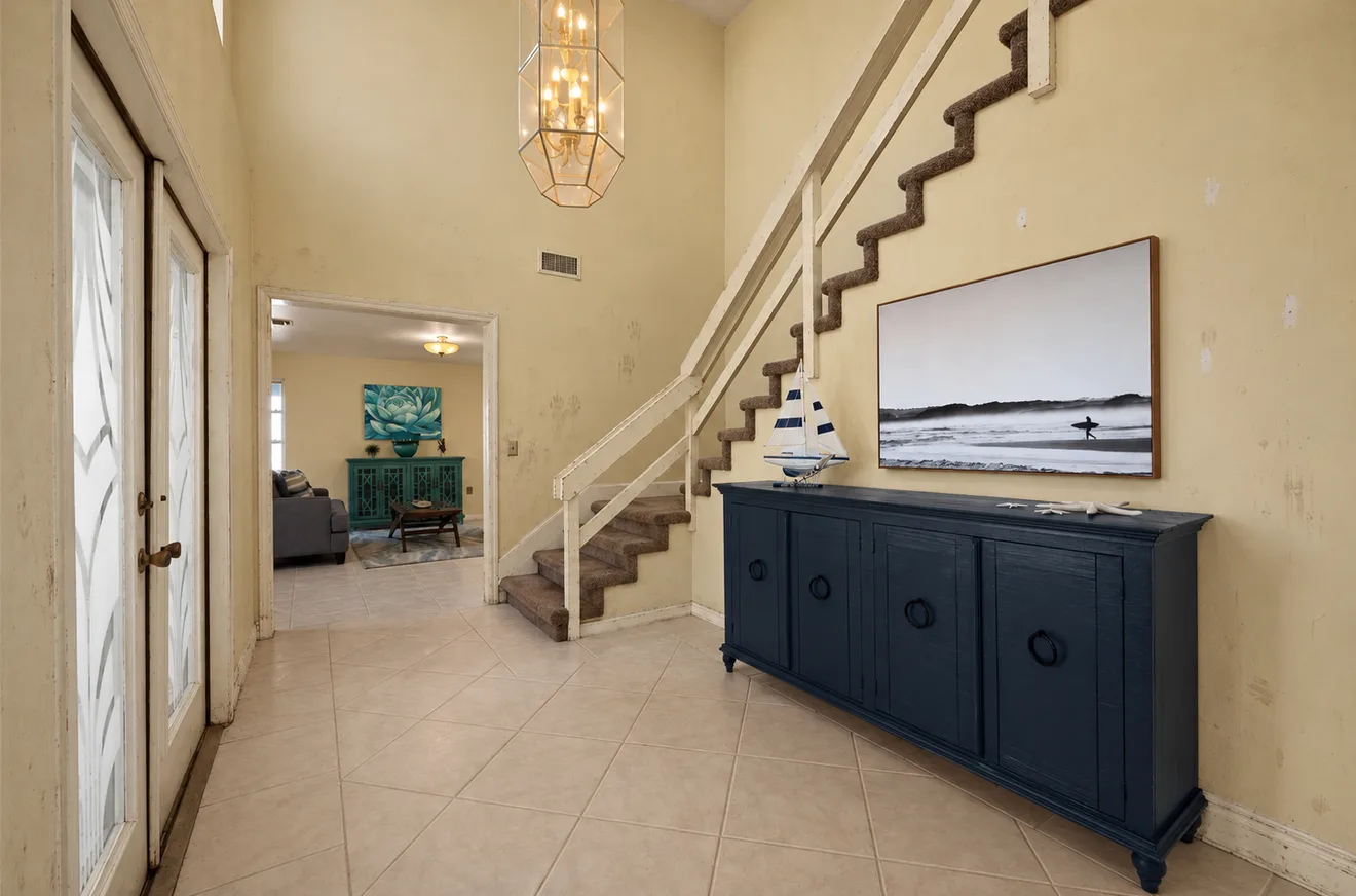 The same foyer before: dingy yellowed walls, scuffed trim and a chipped stair railing